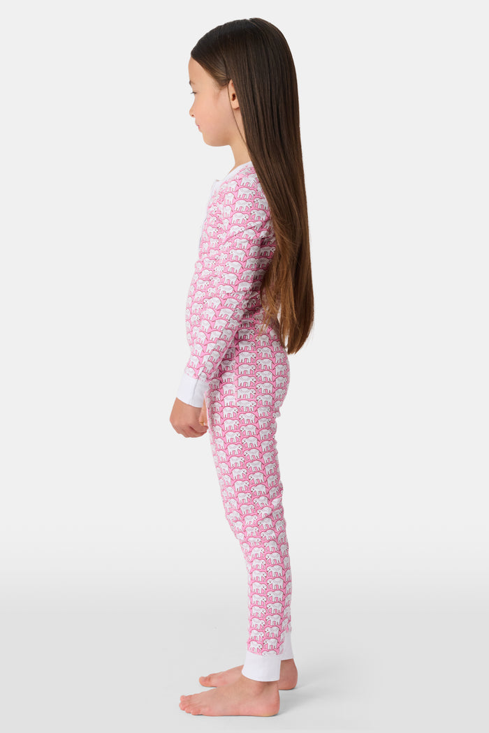 A girl stands barefoot wearing Roller Rabbit Kids Hathi Pajamas—a pink and white, long-sleeve, full-length set with white cuffs and a buttoned neckline—against a plain light background.