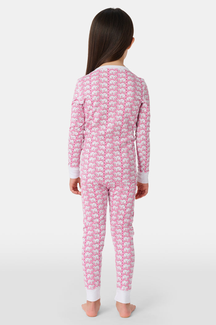 A girl stands barefoot wearing Roller Rabbit Kids Hathi Pajamas—a pink and white, long-sleeve, full-length set with white cuffs and a buttoned neckline—against a plain light background.