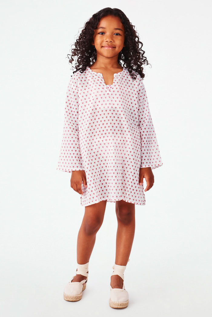A young girl with curly hair smiles in a Roller Rabbit Kids Hearts Kurta, paired with light-colored shoes, standing against a plain white background.