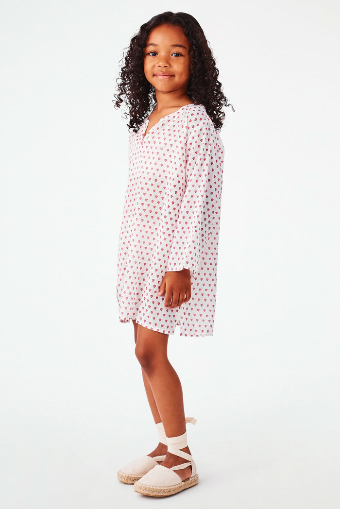 A young girl with curly hair smiles in a Roller Rabbit Kids Hearts Kurta, paired with light-colored shoes, standing against a plain white background.