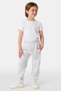A young child smiles while wearing Roller Rabbit Kids Hearts Sweatpants and a plain white t-shirt, with one hand in the pocket and looking slightly to the side.