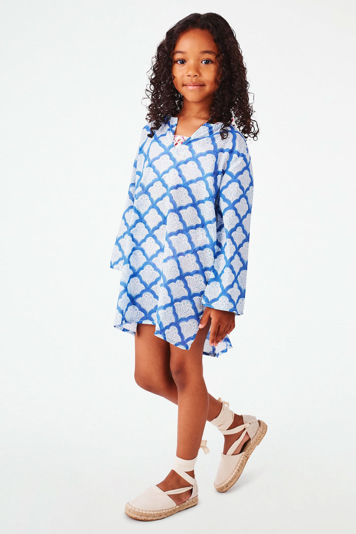A young girl with curly hair smiles against a white background, wearing the Roller Rabbit Kids Jemina Kurta in blue and white cotton, paired with white espadrille sandals.