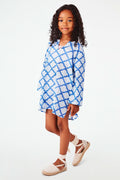 A young girl with curly hair smiles against a white background, wearing the Roller Rabbit Kids Jemina Kurta in blue and white cotton, paired with white espadrille sandals.
