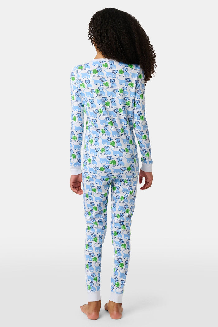 A young child with curly hair stands barefoot, smiling in Roller Rabbit Kids Leo The Lion Pajamas made from soft Pima cotton, against a plain white background.