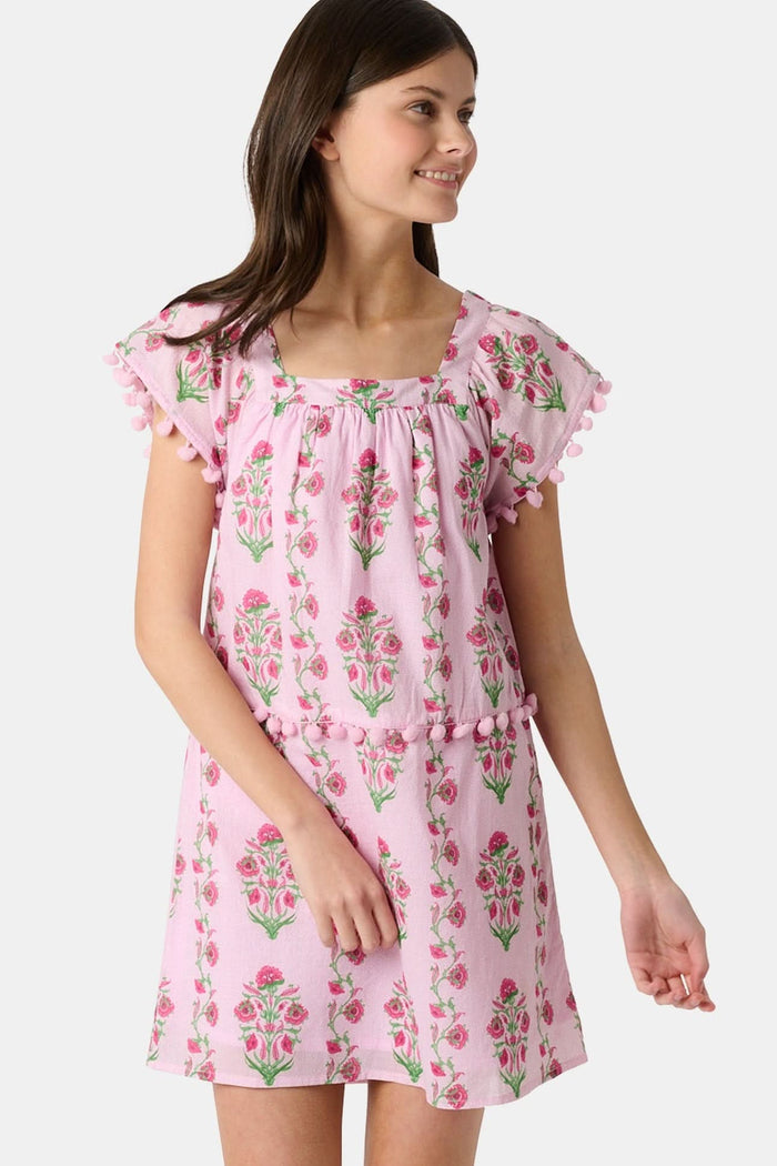 A young girl with long brown hair smiles, wearing the Roller Rabbit Kids Lily Stripe Oceana Dress. She stands with her hands on her hips against a plain light background.