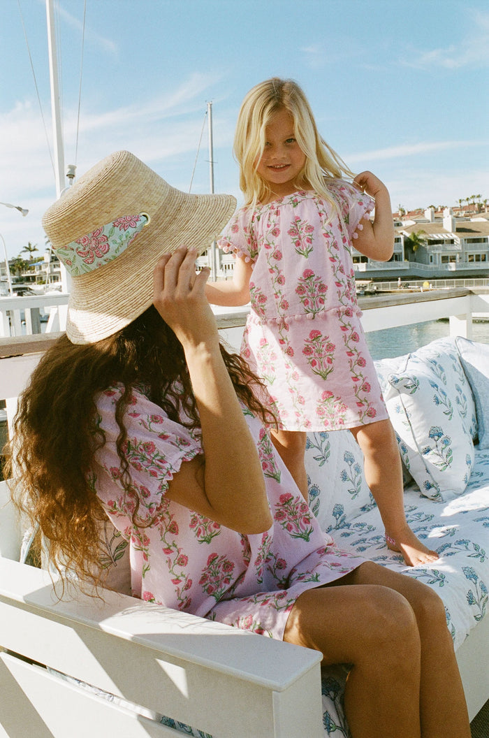 A young girl with long brown hair smiles, wearing the Roller Rabbit Kids Lily Stripe Oceana Dress. She stands with her hands on her hips against a plain light background.