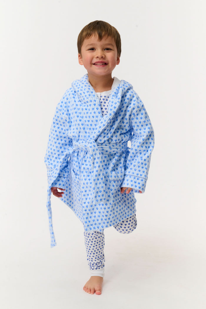 A young child smiles while standing on one leg, wearing the Roller Rabbit Kids Lovely Stripe Max Bathrobe with matching pajamas, in light blue and white, against a plain white background.
