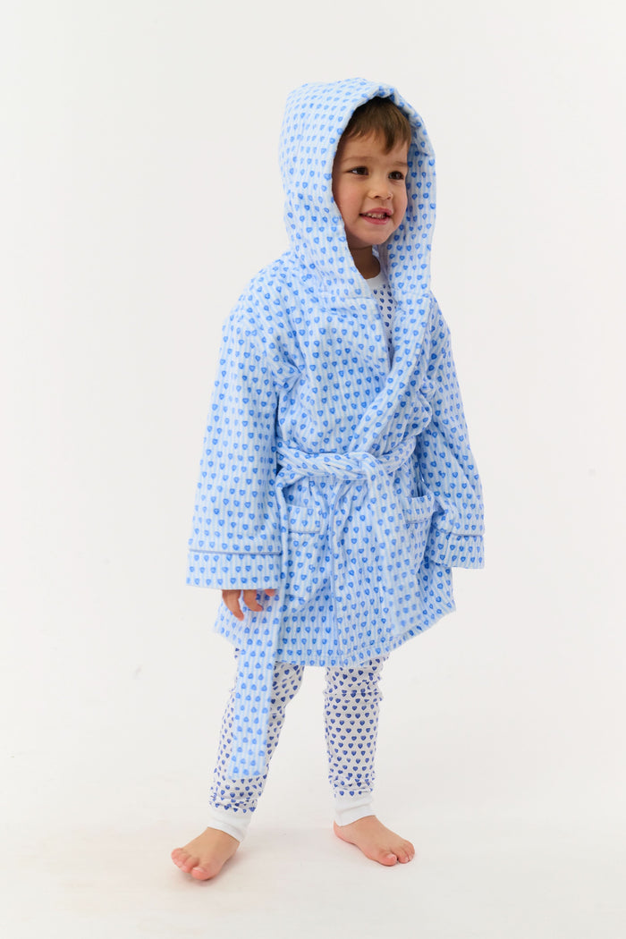 A young child smiles while standing on one leg, wearing the Roller Rabbit Kids Lovely Stripe Max Bathrobe with matching pajamas, in light blue and white, against a plain white background.