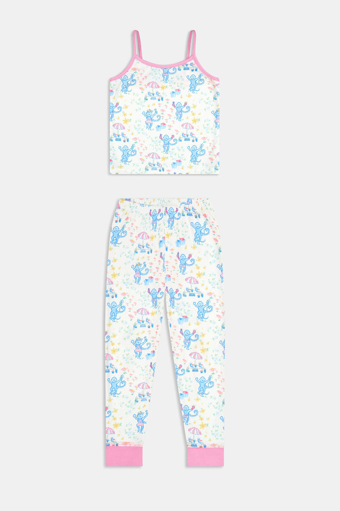 A young girl smiles barefoot against a white background, wearing the Roller Rabbit Kids May Flowers Noa Set—light Pima Cotton pajamas trimmed in pink with a playful floral print.