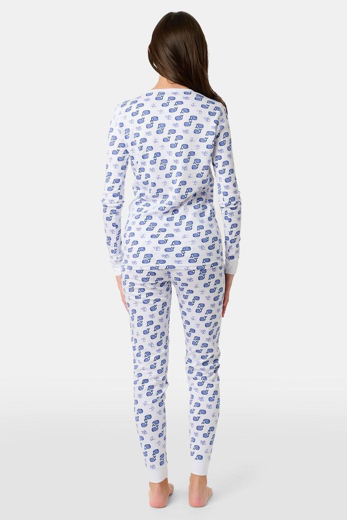 A young boy stands barefoot and smiling in Roller Rabbit's Kids Moby Pajamas—white Pima cotton pajamas with blue car prints, featuring long sleeves and pants—against a plain white background.