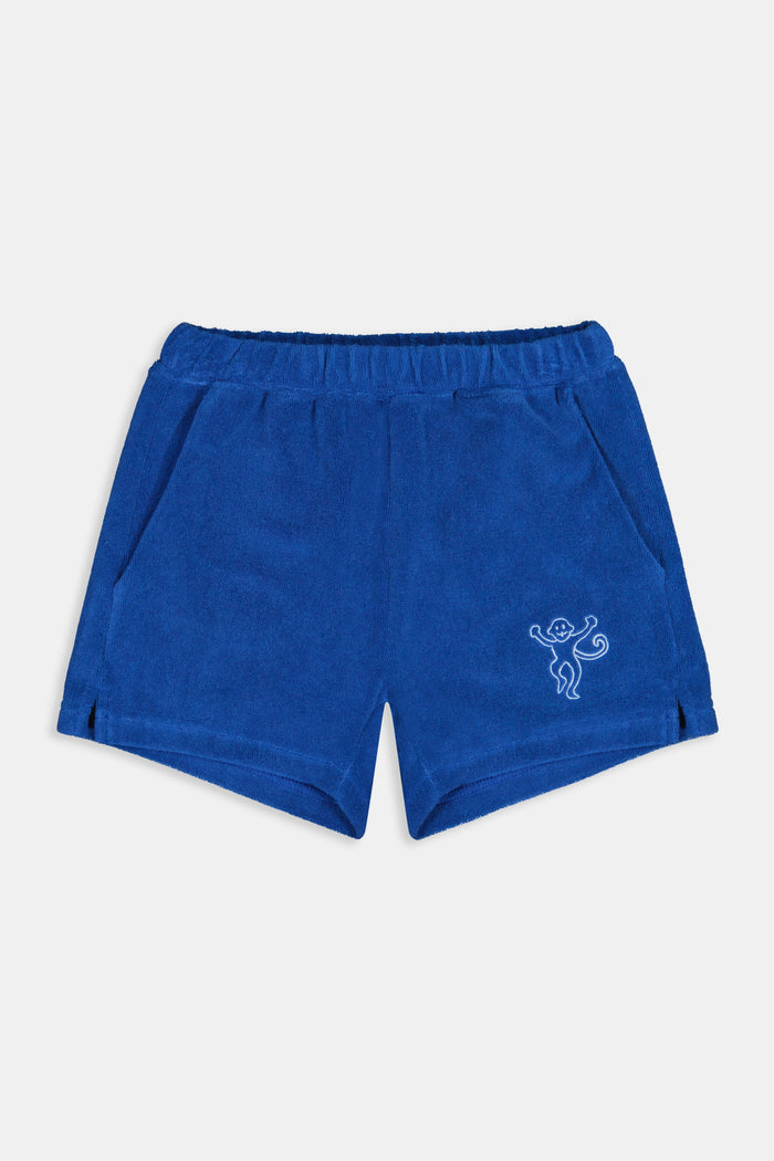 A child wears Roller Rabbit’s Kids Monkey Embroidery Hanni Short in navy with an embroidered figure on the left leg, matching blue top, and white velcro sneakers. Perfect summer shorts for active days.