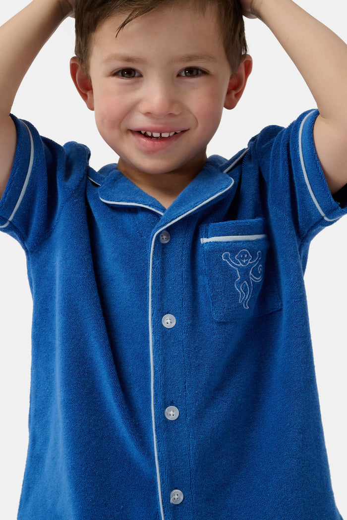A young child wearing the Roller Rabbit Kids Monkey Embroidery Leo Polo—a navy top with white trim and an embroidered monkey on the chest pocket—smiles with arms raised overhead.
