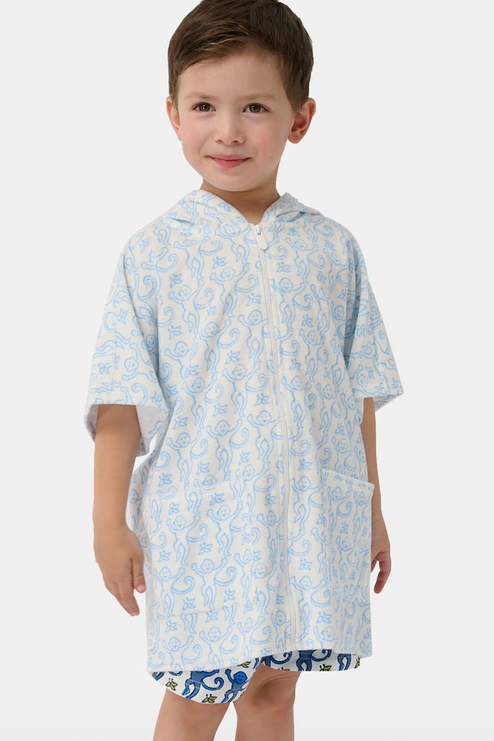A young child smiles at the camera while wearing the Roller Rabbit Kids Monkey Jesse Cover Up, a white terry zip-up onesie with light blue animal prints and a hood.
