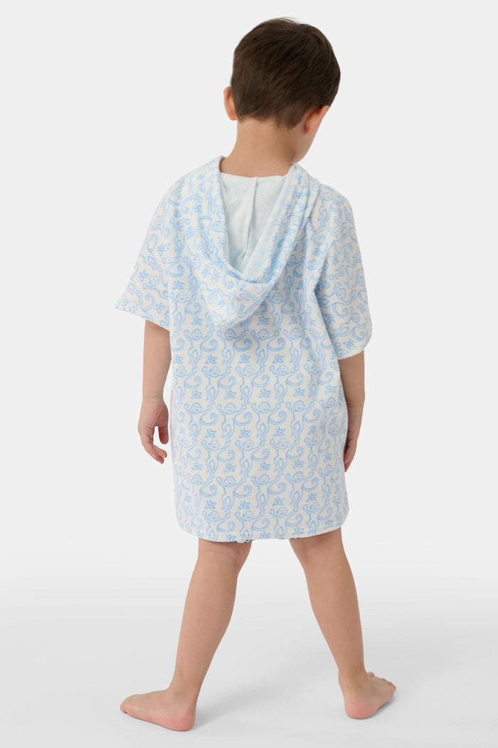 A young child smiles at the camera while wearing the Roller Rabbit Kids Monkey Jesse Cover Up, a white terry zip-up onesie with light blue animal prints and a hood.
