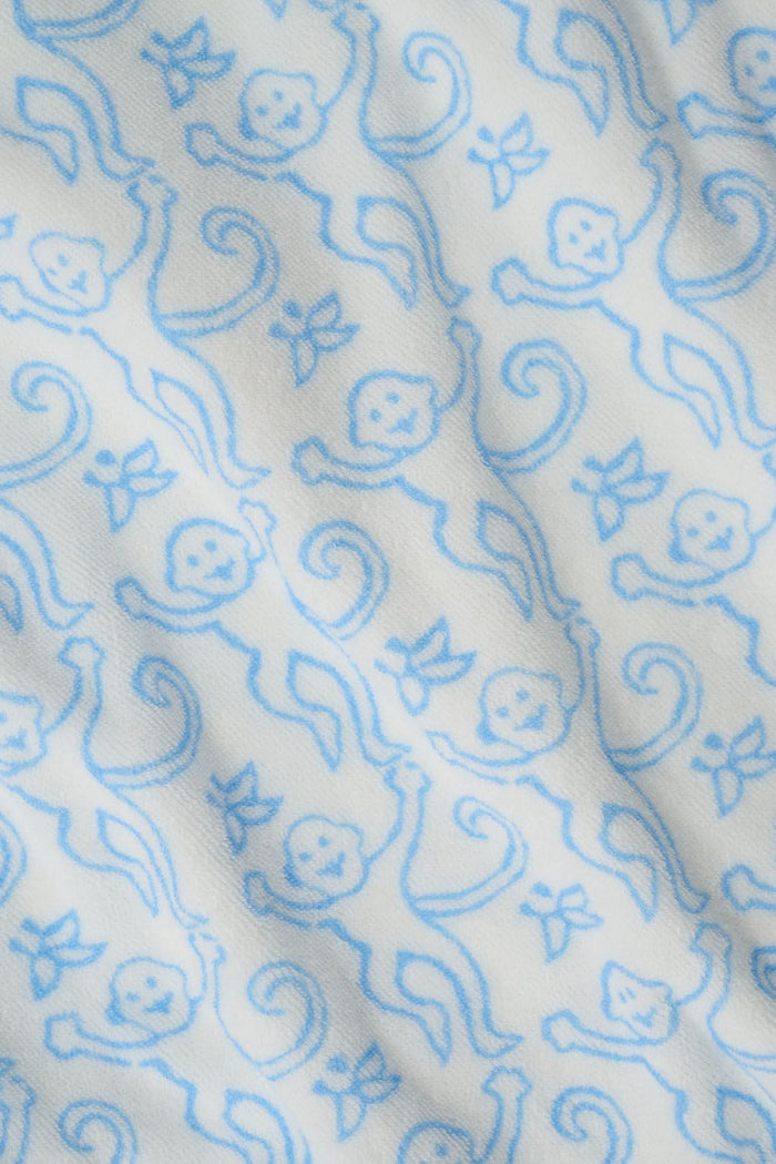 A young child smiles at the camera while wearing the Roller Rabbit Kids Monkey Jesse Cover Up, a white terry zip-up onesie with light blue animal prints and a hood.