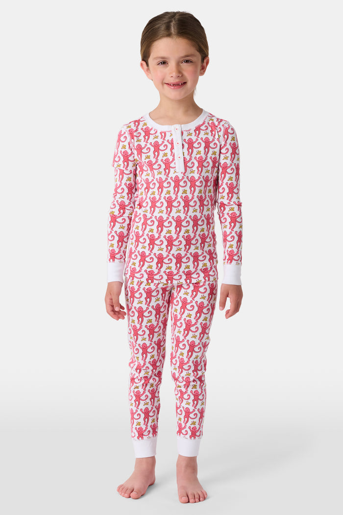 A young child smiles in Roller Rabbit Kids Monkey Pajamas—a matching long-sleeve, full-length set made from 100 Pima cotton with a playful monkey pattern and white cuffs, set against a plain white background.
