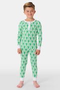 A young boy with light brown hair smiles barefoot in Roller Rabbit’s Kids Monkey Pajamas—a matching 100 cotton set with playful monkey print, white cuffs, and a buttoned neckline—against a plain white background.