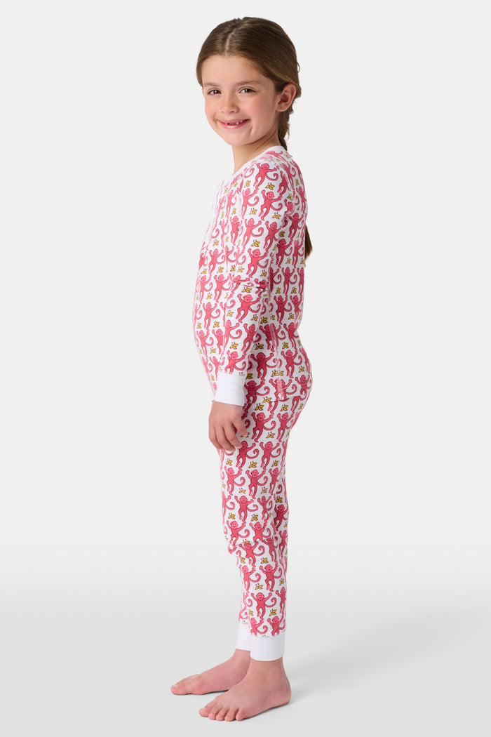 A young child smiles in Roller Rabbit Kids Monkey Pajamas—a matching long-sleeve, full-length set made from 100 Pima cotton with a playful monkey pattern and white cuffs, set against a plain white background.