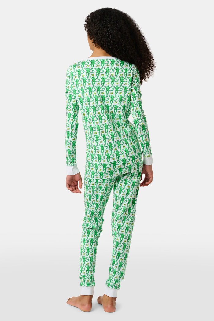 A young boy with light brown hair smiles barefoot in Roller Rabbit’s Kids Monkey Pajamas—a matching 100 cotton set with playful monkey print, white cuffs, and a buttoned neckline—against a plain white background.