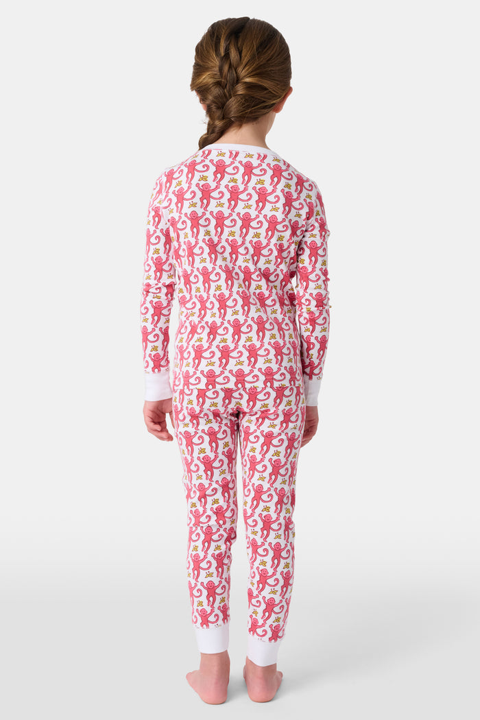 A young child smiles in Roller Rabbit Kids Monkey Pajamas—a matching long-sleeve, full-length set made from 100 Pima cotton with a playful monkey pattern and white cuffs, set against a plain white background.