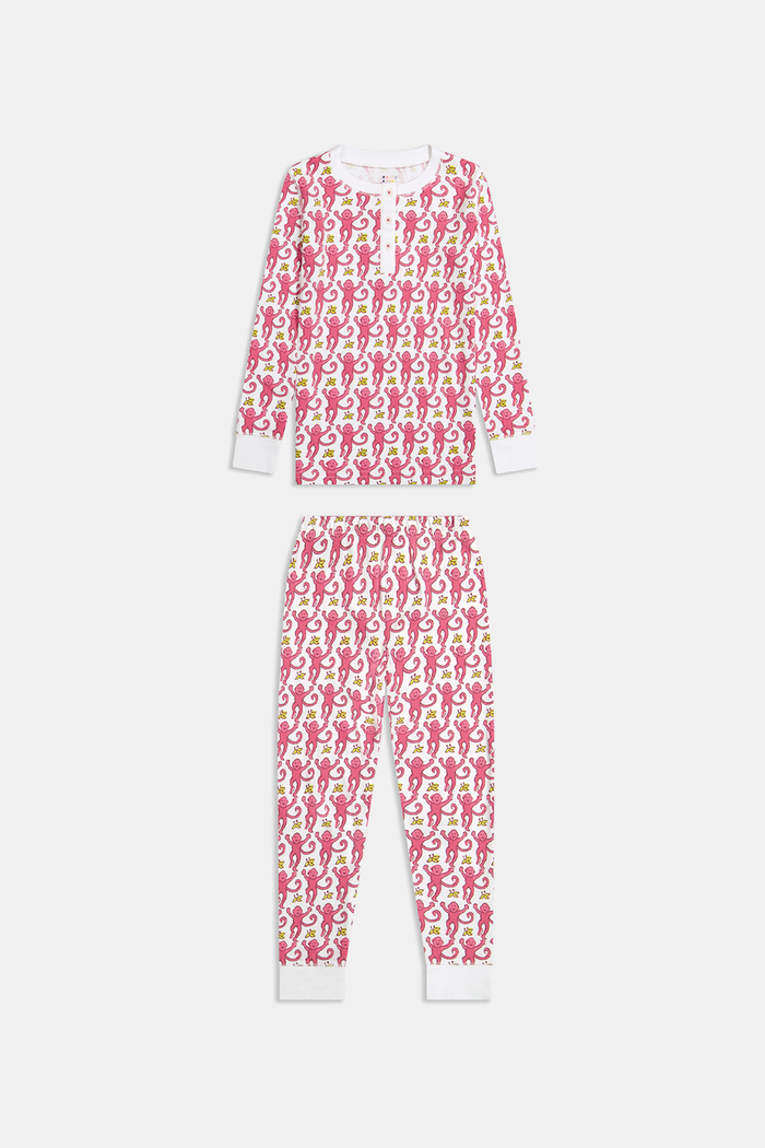 A young child smiles in Roller Rabbit Kids Monkey Pajamas—a matching long-sleeve, full-length set made from 100 Pima cotton with a playful monkey pattern and white cuffs, set against a plain white background.