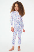 A young girl with curly hair stands barefoot, wearing Roller Rabbit Kids Nantucket Memories Pajamas crafted from soft Pima cotton, featuring a colorful whimsical print, set against a simple white background.