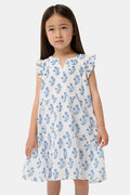 A young girl with long brown hair wears the Roller Rabbit Kids Rosa Ditsy Floral Pami Dress, made from cotton voile with blue-green block print and ruffled sleeves, standing against a plain light background, looking slightly to the side.