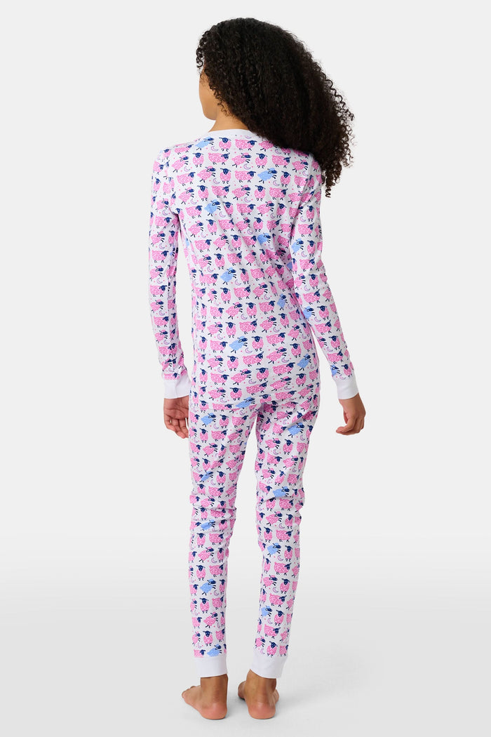 A smiling young girl stands barefoot in Kids Sammy The Sheep Pajamas by Roller Rabbit, posing against a white backdrop to showcase stylish children's sleepwear.