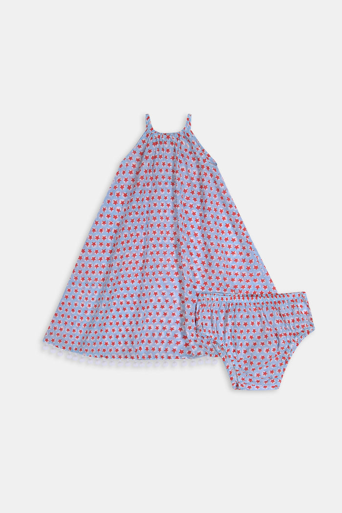 A young girl with long brown hair stands facing forward in the Roller Rabbit Kids Starry Dot Carrie Cover Up—a sleeveless, knee-length white dress featuring a red dotted pattern and pom-pom trim. She has a neutral expression and a light background behind her.