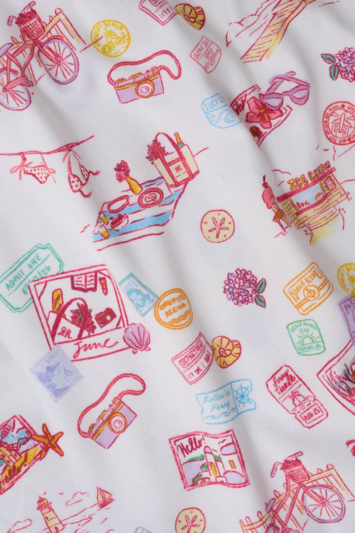 A woman with curly hair models the Roller Rabbit Summer Memories Fiora Pajamas, a Pima cotton set with a colorful sushi print, including a short-sleeve button-up top and long pants, against a white background.