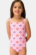 A young girl with long brown hair smiles in the Roller Rabbit Kids Sunny Days Rory One Piece, featuring ruffled straps and full coverage with orange and purple sun and palm tree patterns, against a plain light background.