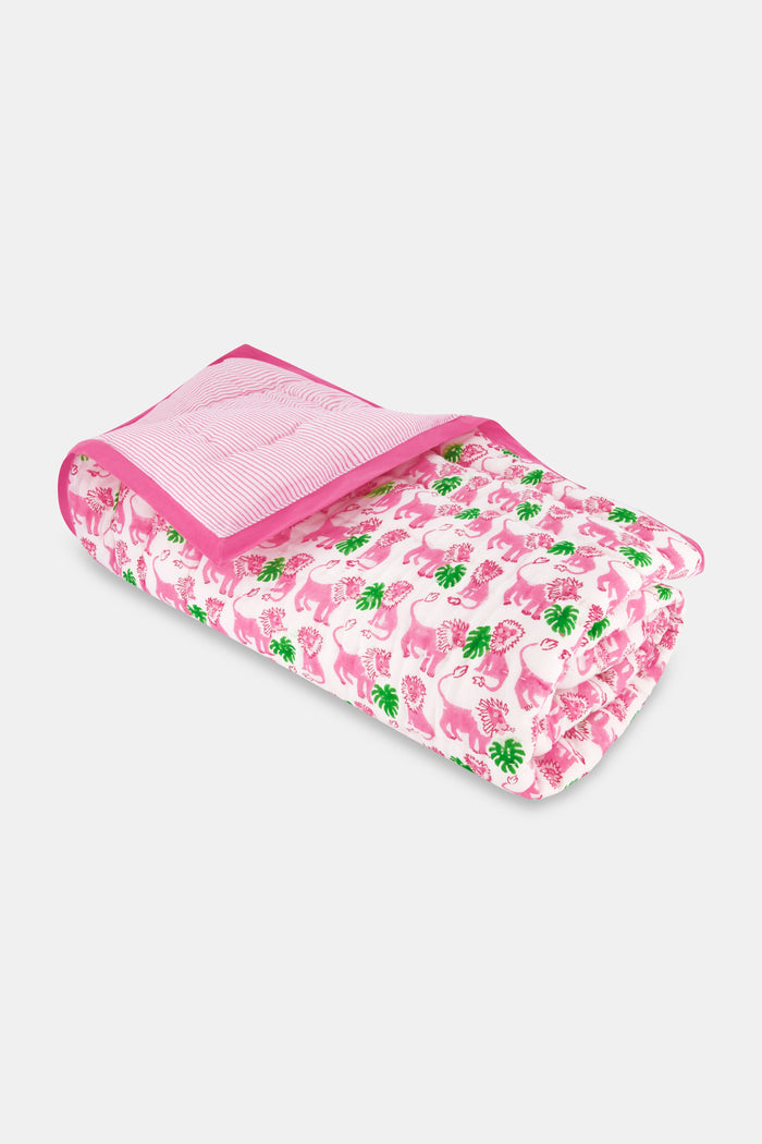 The Roller Rabbit Leo the Lion Baby Quilt features a soft cotton design with a pink border, white background, and playful pattern of pink elephants and green palm trees. A striped pink lining is visible along the folded edge.