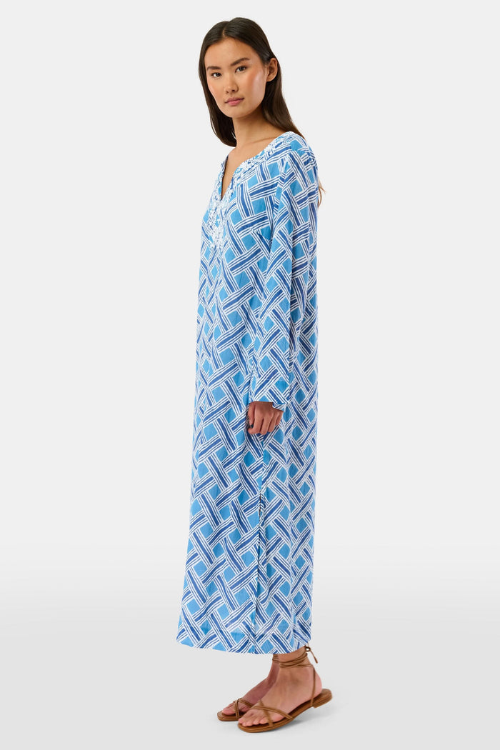 A woman stands in sandals against a white background wearing the Roller Rabbit Liana Astrella Kurta, a blue and white patterned, maxi-length cotton kurta with a V-neck and ruffle detailing.