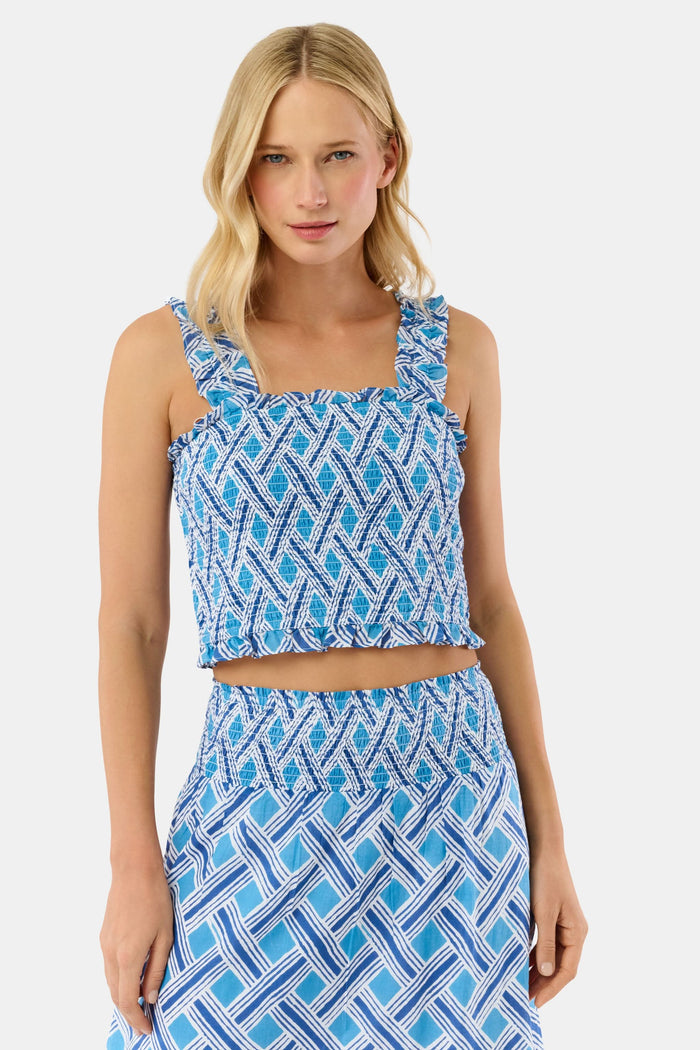 A woman with blonde hair wears the Roller Rabbit Liana Sabrina Top, a smocked cotton piece with blue and white patterns and ruffled straps, paired with a matching high-waisted skirt, standing against a plain white background.