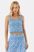 A woman with blonde hair wears the Roller Rabbit Liana Sabrina Top, a smocked cotton piece with blue and white patterns and ruffled straps, paired with a matching high-waisted skirt, standing against a plain white background.