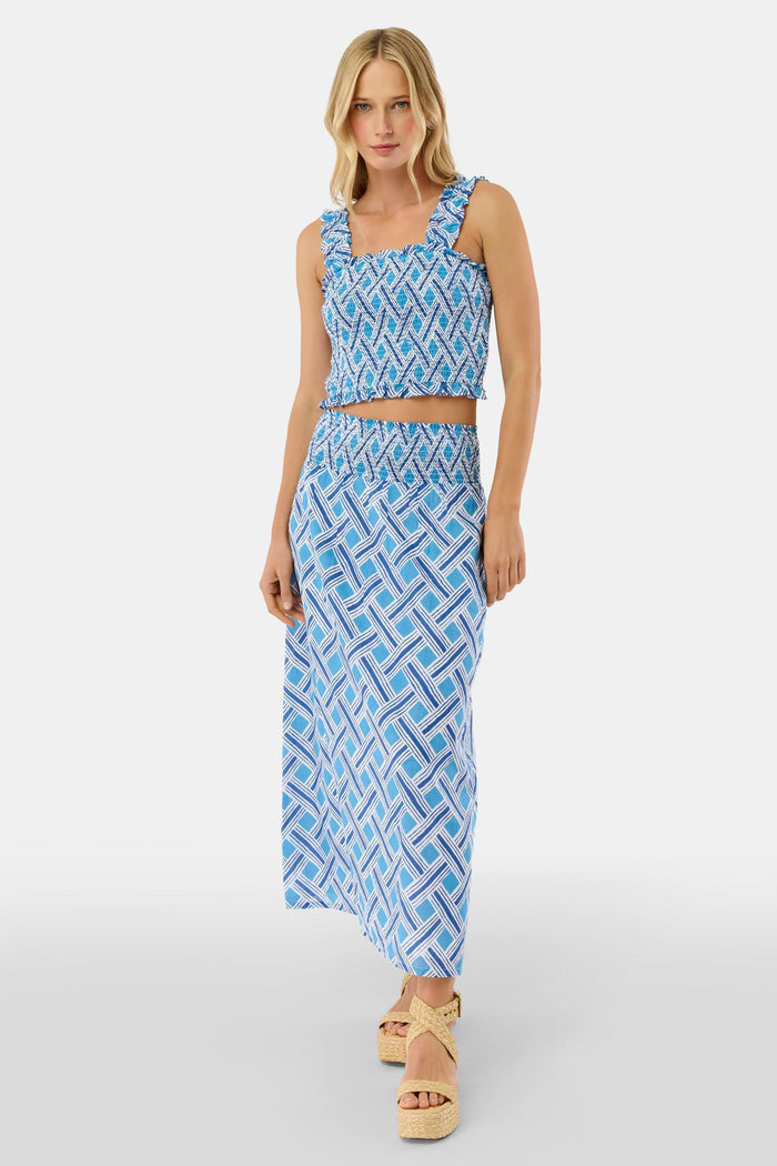 A woman with blonde hair wears the Roller Rabbit Liana Sabrina Top, a smocked cotton piece with blue and white patterns and ruffled straps, paired with a matching high-waisted skirt, standing against a plain white background.