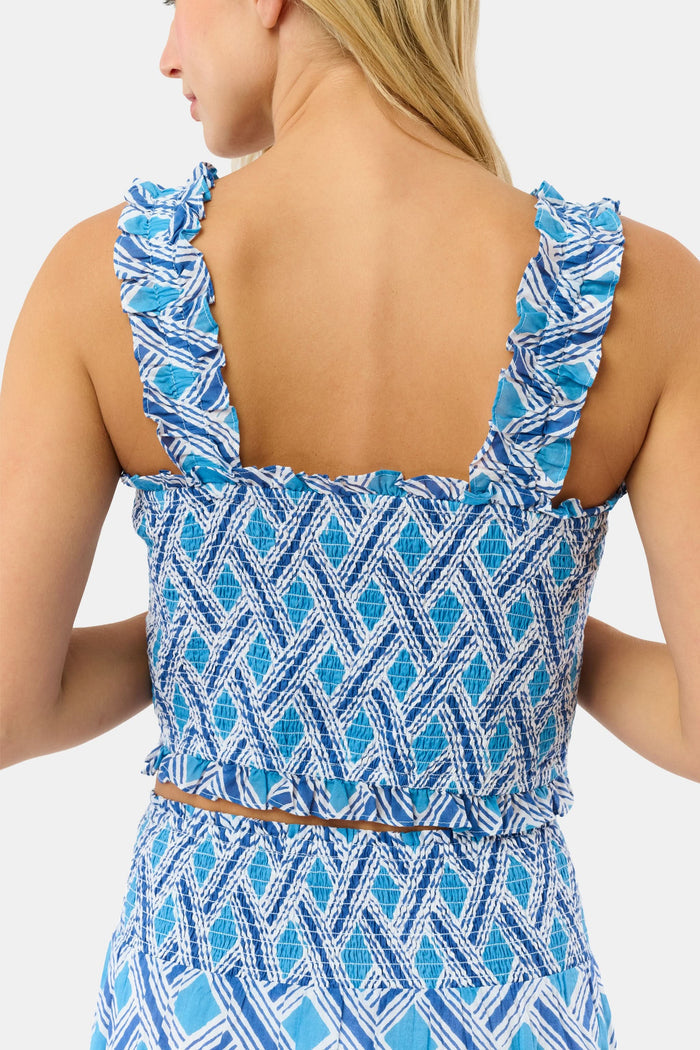 A woman with blonde hair wears the Roller Rabbit Liana Sabrina Top, a smocked cotton piece with blue and white patterns and ruffled straps, paired with a matching high-waisted skirt, standing against a plain white background.