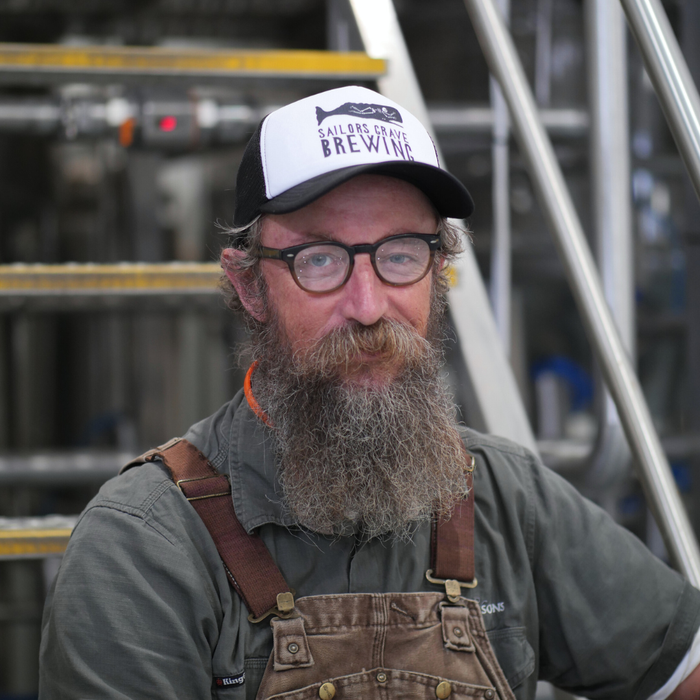 Sailors Grave Brewing Chris Moore wearing a logo cap and overalls in a brewery setting