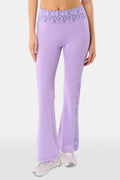 A person wears Roller Rabbit’s Lovely Monkey Ally Flared Leggings—lavender with a patterned waistband and side panels—paired with white sneakers, standing against a plain white background.