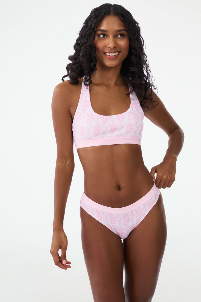 A person wears a light pink pima modal bra and the Roller Rabbit Lovely Monkey Hudson Bikini panty with a cheeky monkey print, standing with hands on hips against a plain background.