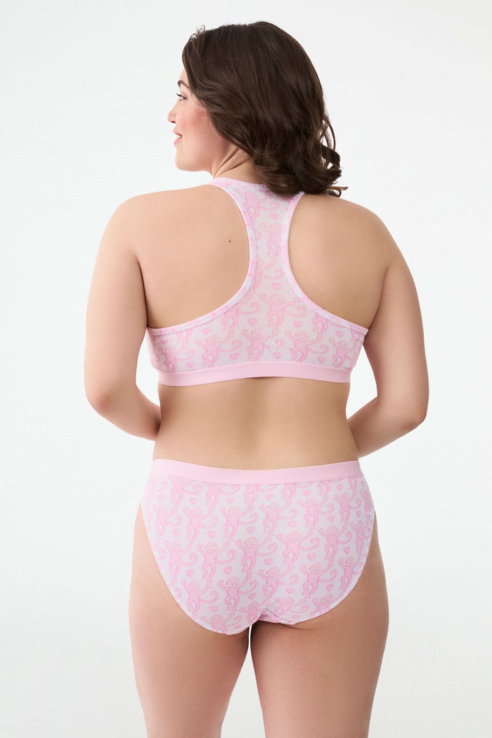 A person wears a light pink pima modal bra and the Roller Rabbit Lovely Monkey Hudson Bikini panty with a cheeky monkey print, standing with hands on hips against a plain background.