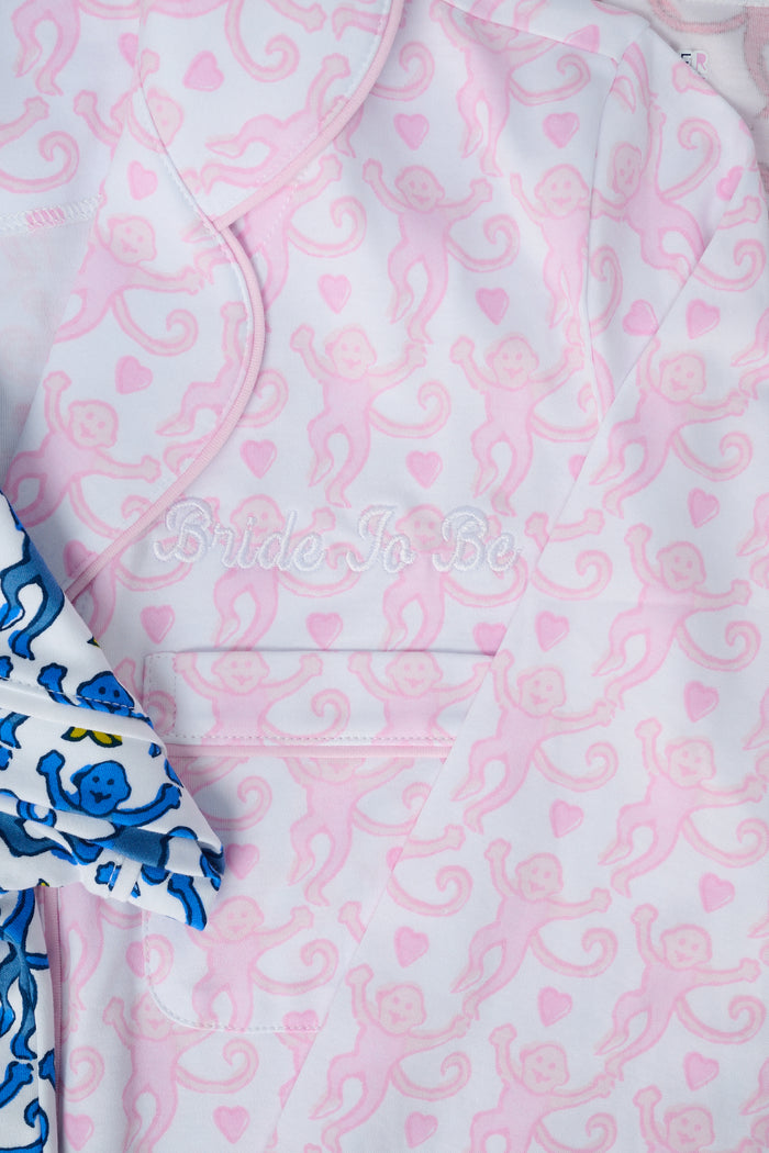 A woman with light brown hair and a neutral expression stands barefoot on a white background wearing Roller Rabbit's Lovely Monkey Long Sleeve Polo Pajamas, a light pink and white 100 Pima Cotton set.