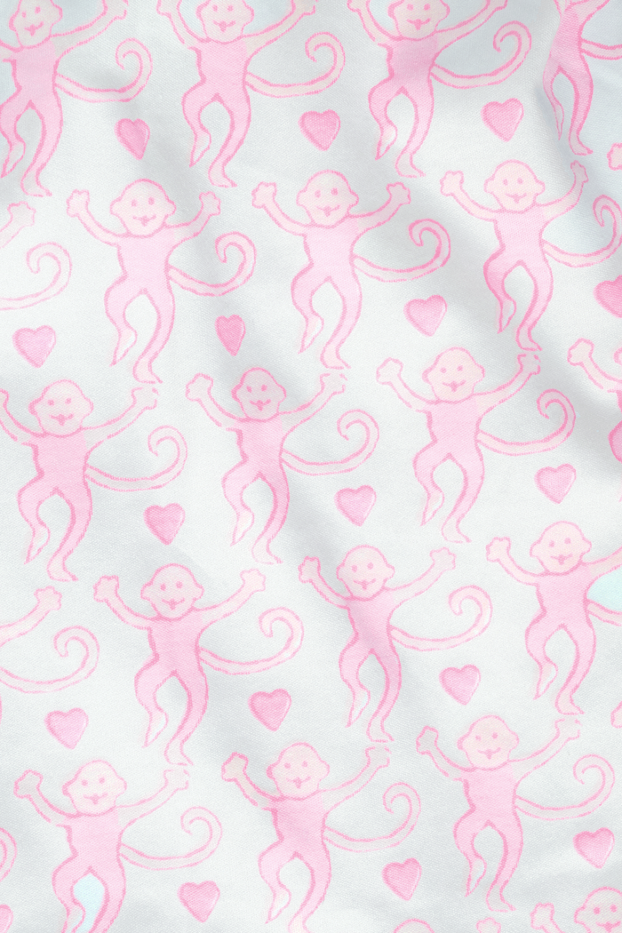 A woman with light brown hair and a neutral expression stands barefoot on a white background wearing Roller Rabbit's Lovely Monkey Long Sleeve Polo Pajamas, a light pink and white 100 Pima Cotton set.