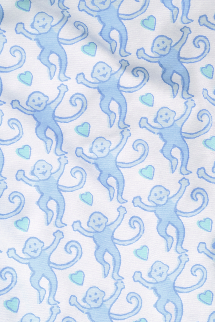 A woman with long blonde hair wears the Roller Rabbit Lovely Monkey Polo Pajamas set in light blue and white Pima cotton shorts, smiling softly against a plain light background.