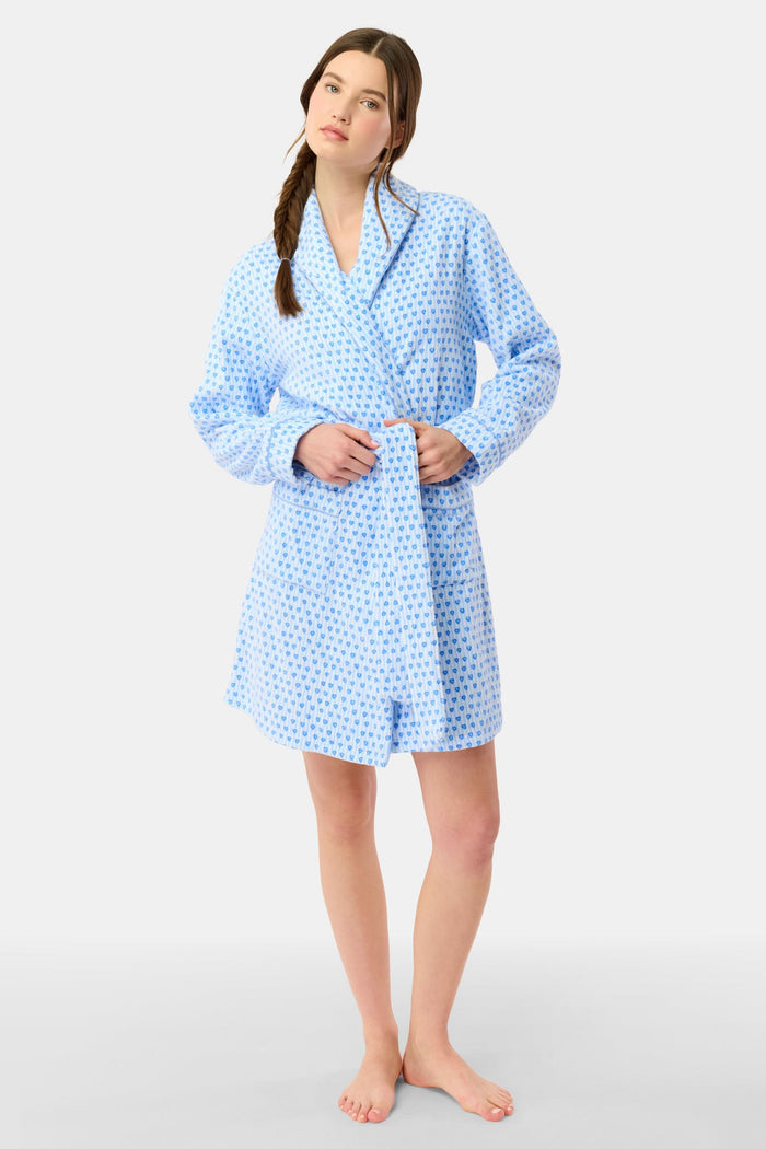 A woman with a side braid wears the Roller Rabbit Lovely Stripe Max Robe, a light blue cotton piece with small blue heart patterns, belt, and large front pockets. She stands against a plain background, looking at the camera neutrally.