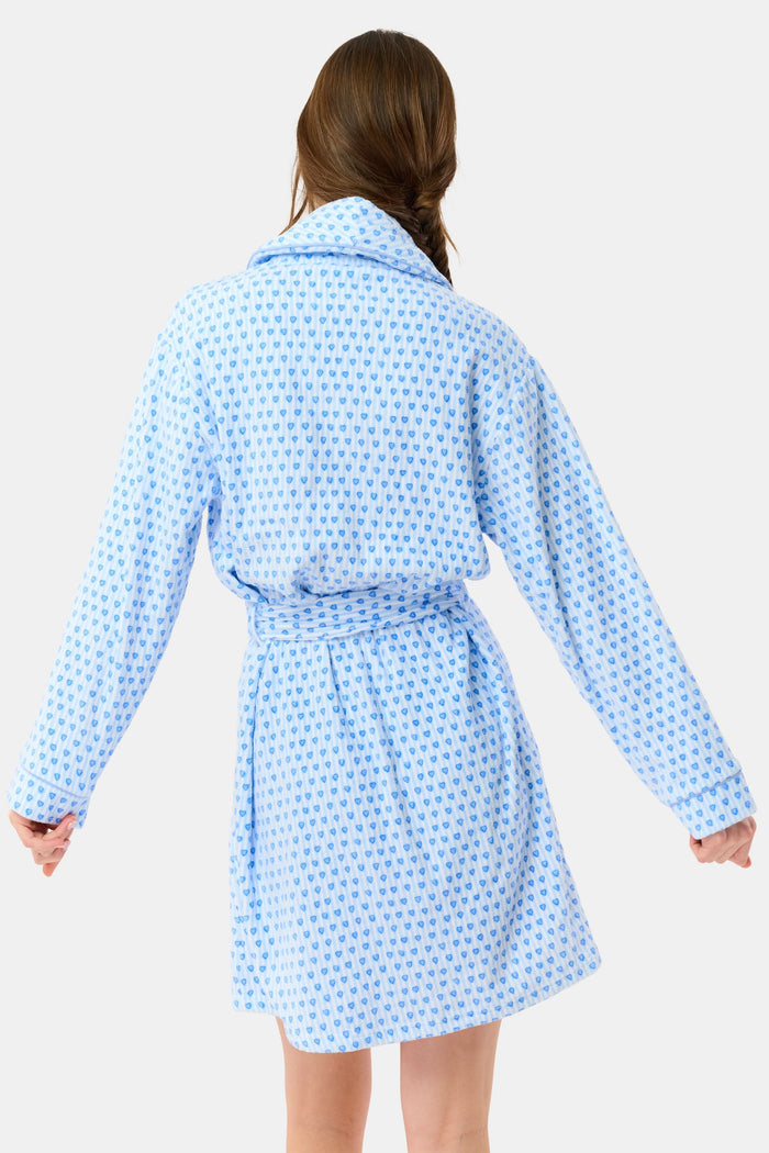 A woman with a side braid wears the Roller Rabbit Lovely Stripe Max Robe, a light blue cotton piece with small blue heart patterns, belt, and large front pockets. She stands against a plain background, looking at the camera neutrally.