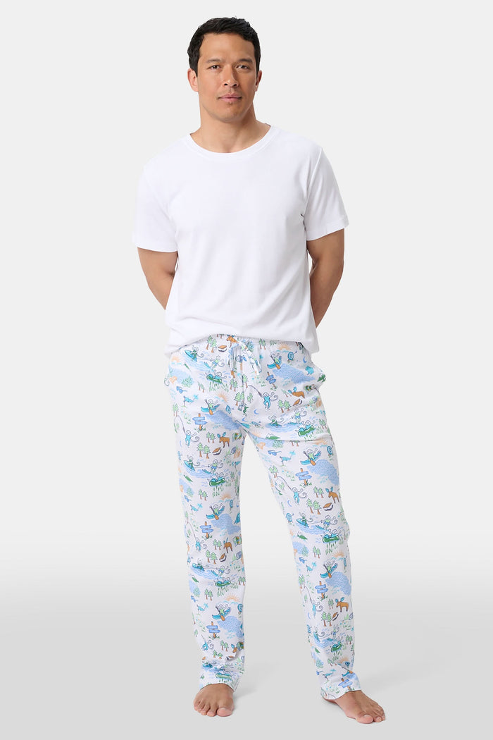 A person wears the Roller Rabbit Mens Camp RR Simon Pant, featuring a colorful animal and nature print, with hands in pockets and a plain white shirt. The barefoot individual stands against a white background.