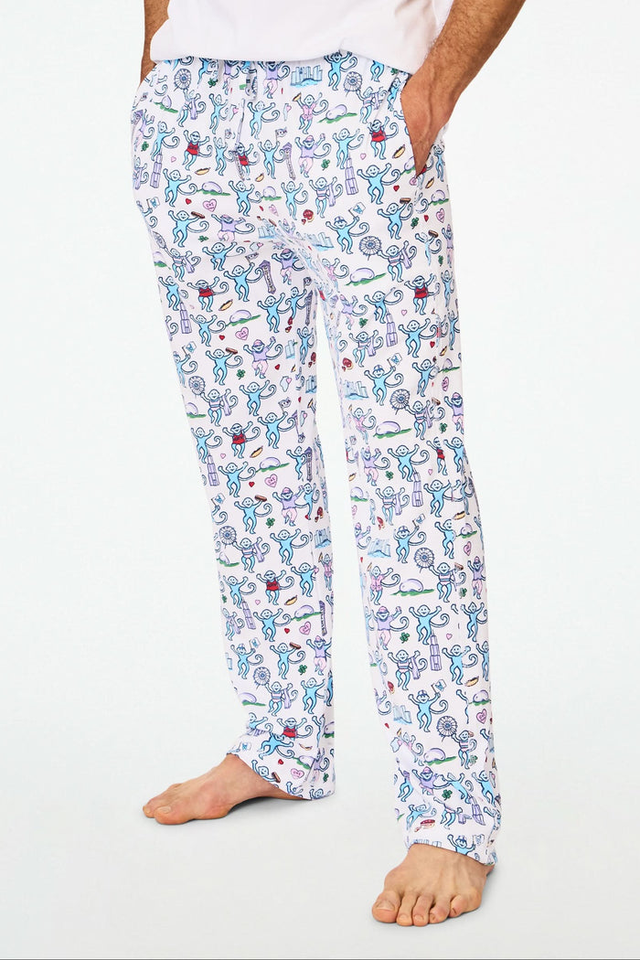 A person stands barefoot in cozy Roller Rabbit Mens Chicago Monkey Simon Pants, featuring a colorful print, paired with a plain white T-shirt. Only the lower half of the body is visible against a white background.