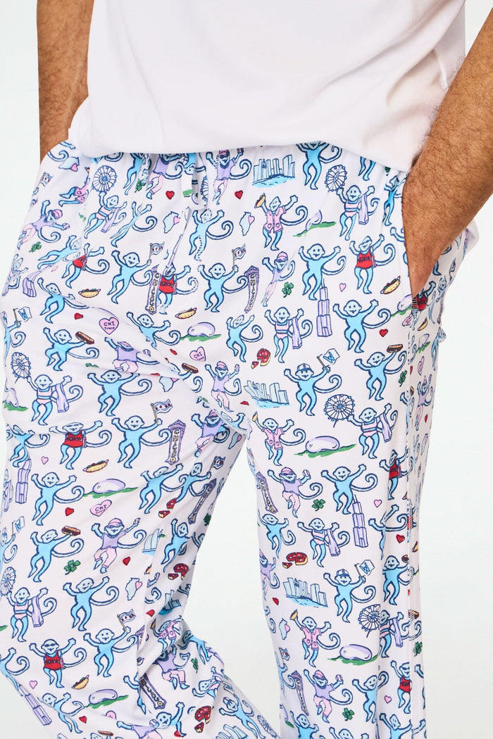 A person stands barefoot in cozy Roller Rabbit Mens Chicago Monkey Simon Pants, featuring a colorful print, paired with a plain white T-shirt. Only the lower half of the body is visible against a white background.