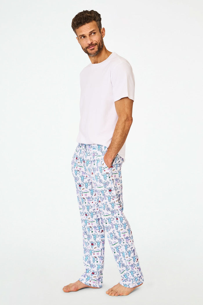 A person stands barefoot in cozy Roller Rabbit Mens Chicago Monkey Simon Pants, featuring a colorful print, paired with a plain white T-shirt. Only the lower half of the body is visible against a white background.